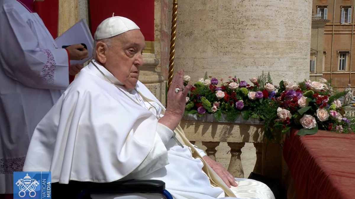 Papa Francisc în scaun cu rotile cu mâna dreaptă ridicată și flori colorate în fundal