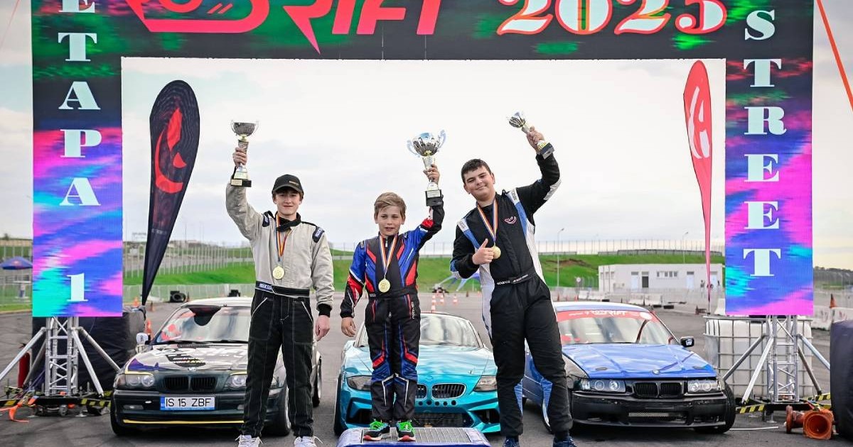 Podiumul unei competiții de drift, unde trei piloți tineri, îmbrăcați în costume de curse, sărbătoresc victoria. În centrul imaginii se află un copil, ținând un trofeu ridicat în mână