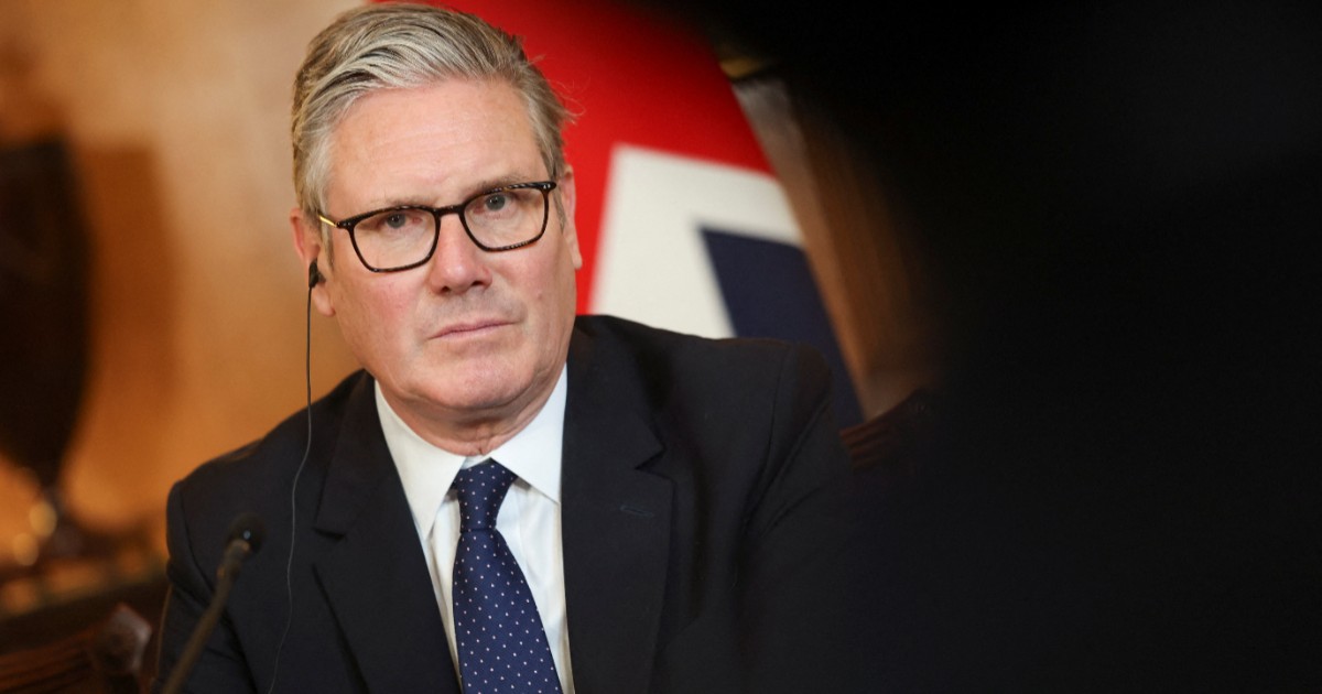 Premierul Keir Starmer cu ochelari, îmbrăcat în costum de culoare neagră, cu steagul Marii Britanii în fundal