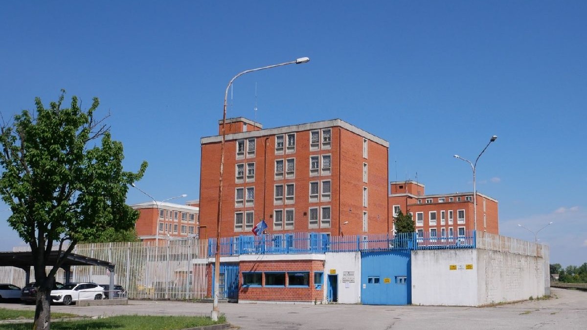 Fotografia înfățișează o clădire mare, din cărămidă roșie. Un gard metalic albastru se întinde pe toată lungimea proprietății.