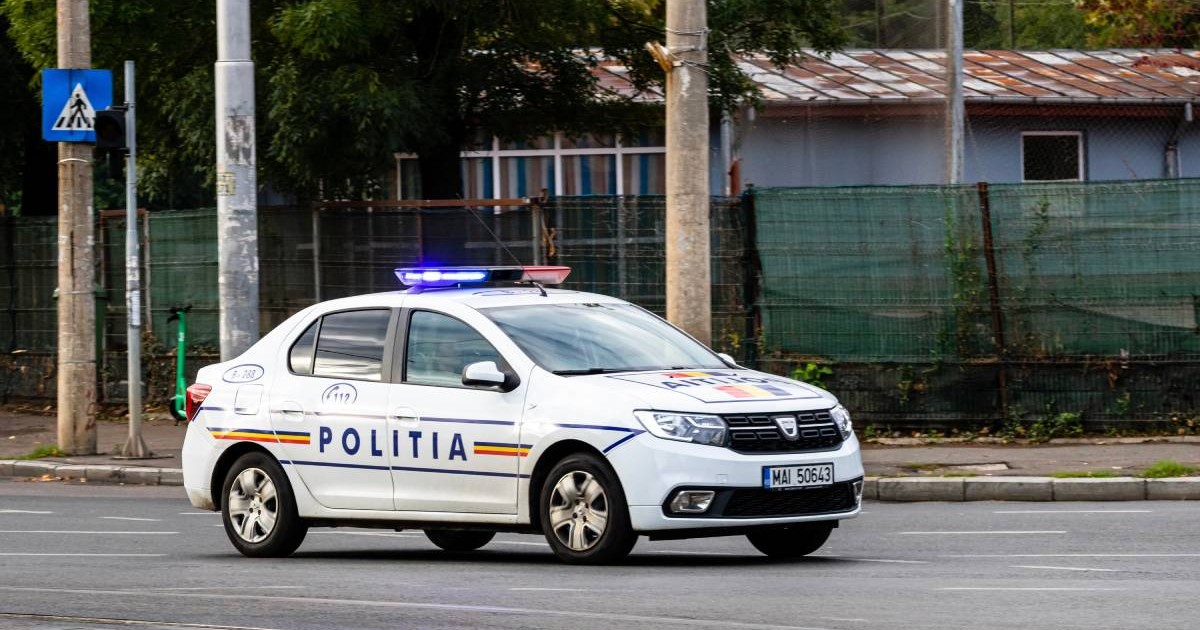 O mașină de poliție mergând pe stradă ziua în oraș cu girofarul pornit