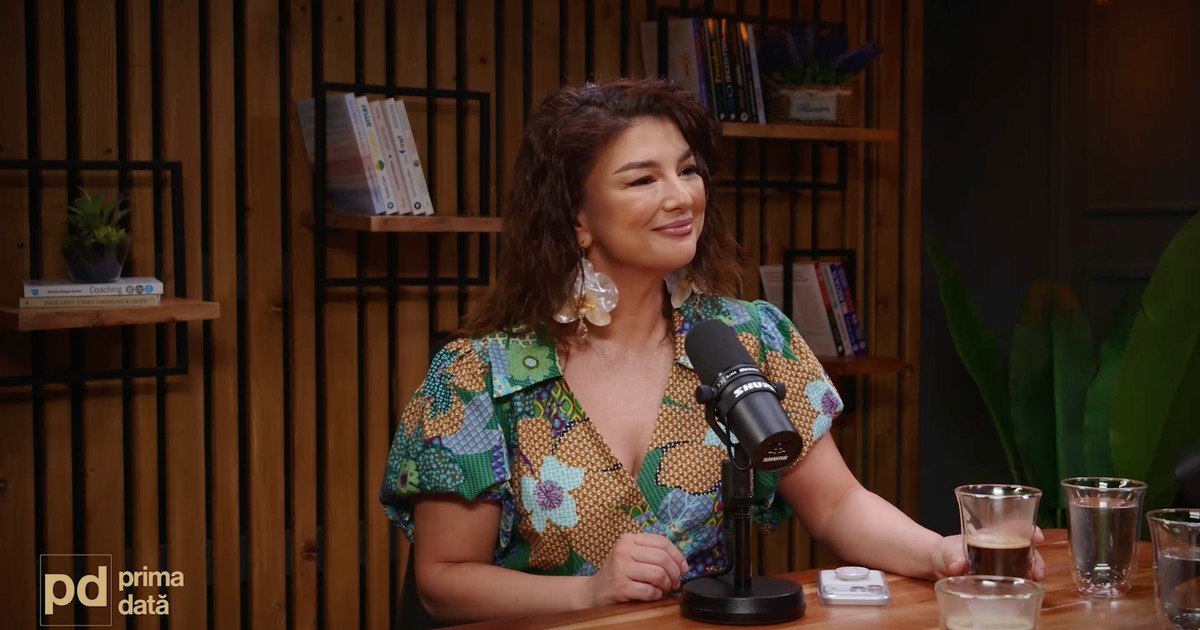 Maria Popovici, în timpul podcastului „Prima dată”, stând la masă, cu un microfon în față, îmbrăcată cu o bluză cu imprimeu floral.