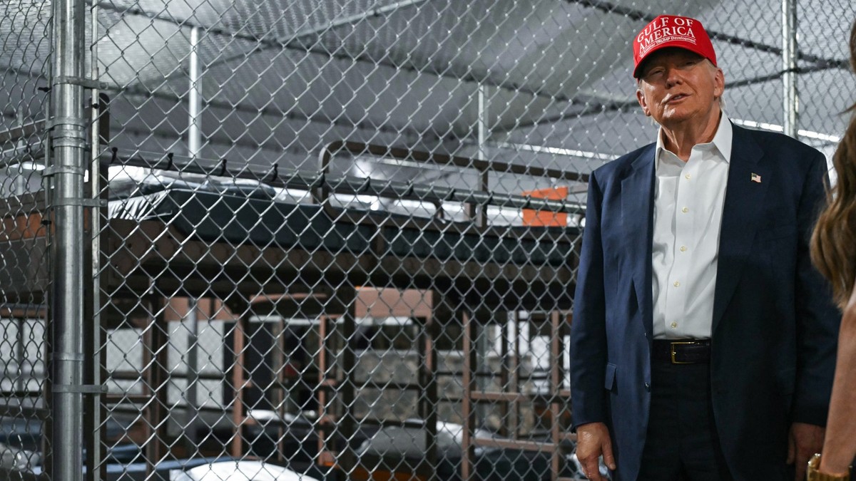 Donald Trump (dreapta) surprins în închisoarea „Alcatrazul aligatorilor”, pe 1 iulie 2025. Poartă o șapcă roșie MAGA, un costum albastru și cu o cămașă albă. În stânga lui se află paturi