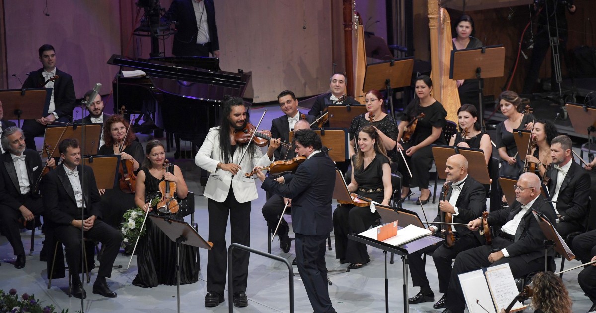 Concertul unei orchestre pe o scenă, cu un dirijor.