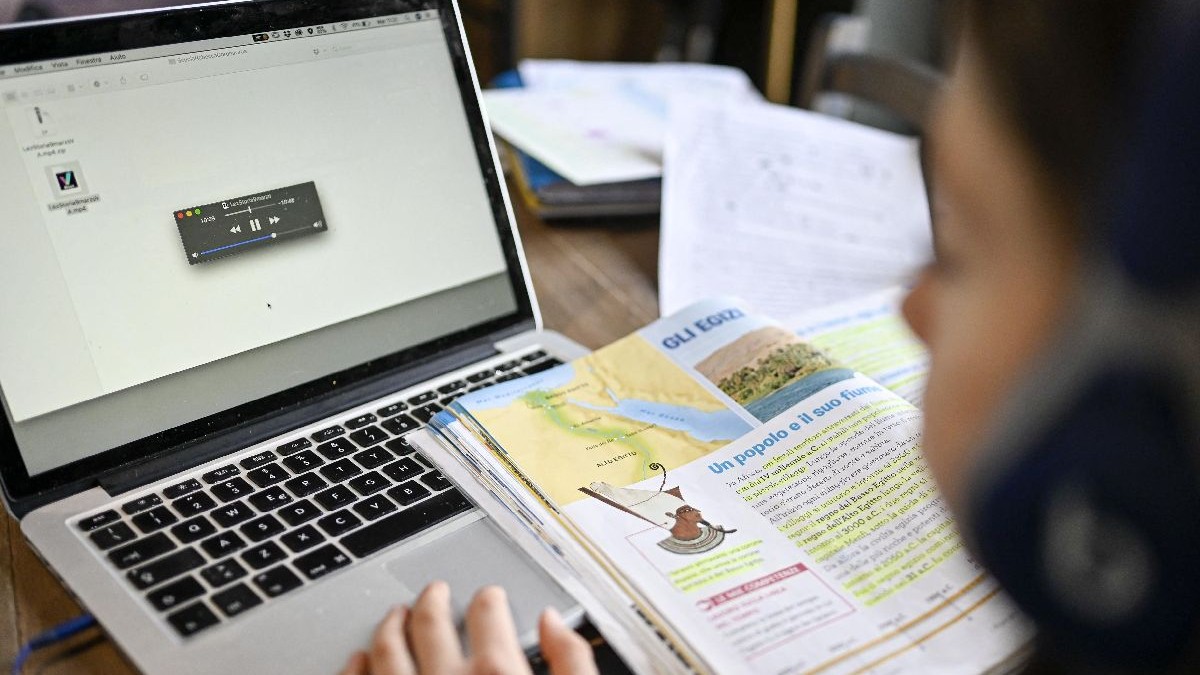 Un elev se uită pe manual, in fata unui laptop