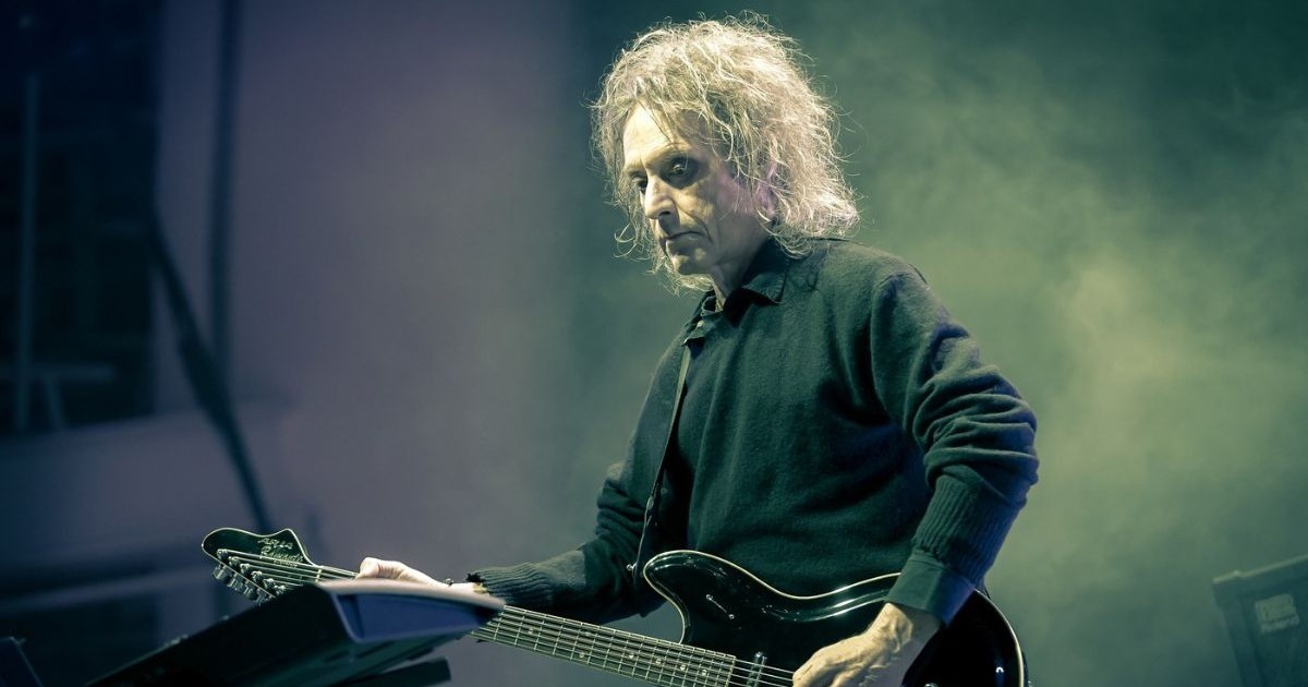 perry bamonte cântând la chitară pe scenă, în timpul unui concert the cure