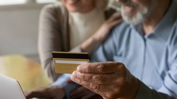 bătrân care ține un card bancar în mână, iar lângă el se află o femeie