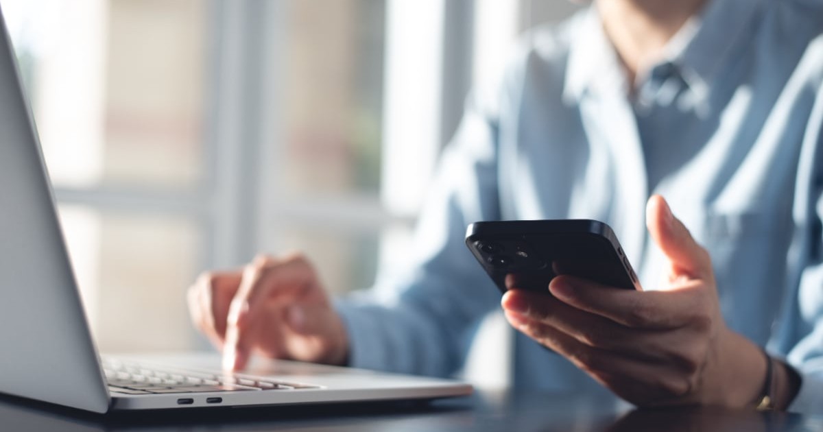 O femeie care se uită în ecranul laptopului și al telefonului mobil, după ce i-a venit factura