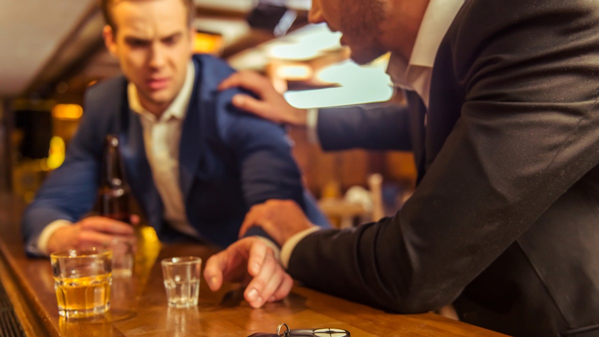 În cât timp iese alcoolul din organism - Imagine cu un bărbat care a consumat alcool şi care este împiedicat de un prieten să plece cu maşina.