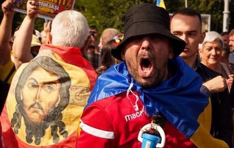 O imagine cu fața lui Isus pe un steag purtat pe spate de un protestatar, langa un al protestatar care tip la protestul fermierilor din Piața Victoriei, de pe 15 septembrie