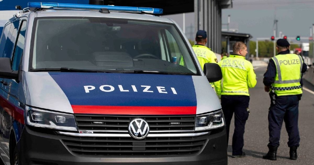 Trei polițiști cu veste reflectorizante stau in picioare, langă o mașină de poliție din Austria