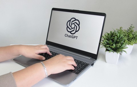 O femeie care scrie pe un laptop. Pe ecran este accesat ChatGPT