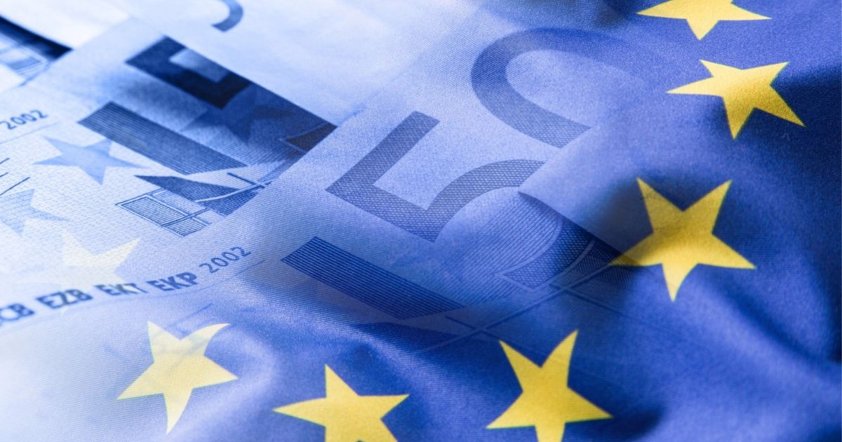 Steagul Uniunii Europene fluturând pe un fundal cu monede euro.