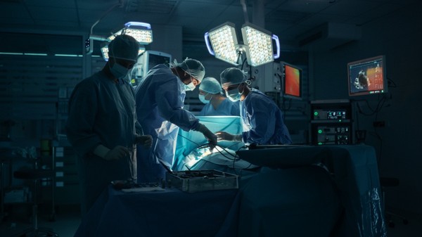 Medici în timpul unei operații, îmbrăcați în costume verzi, în timp ce un pacient este pe masă