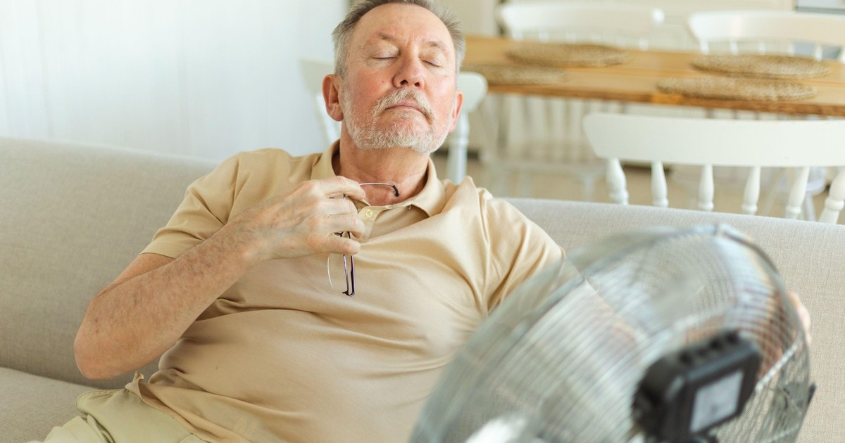 Un bărbat în vârstă se răcorește lângă un ventilator într-o zi toridă din timpul valului de căldură de vară. Un bărbat în vârstă, afectat de căldura verii, încearcă să supraviețuiască cu ajutorul unui ventilator electric.