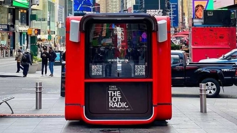 Un chioșc roșu de studio radio pop-up al postului „The Lot Radio”, instalat în spațiul public din Times Square, New York, având difuzoare pe margini și panouri cu coduri QR