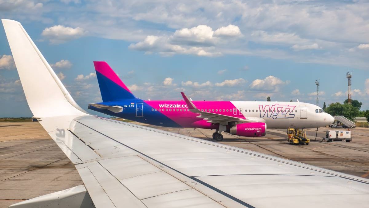 Un avion Wizz Air, colorat cu roz și albastru, stând pe pistă, în timp ce pilotul așteaptă să decoleze