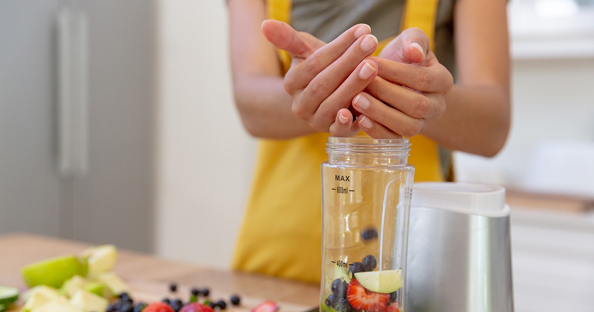 O femeie care face un smoothie la un blender în care pune multe fructe.