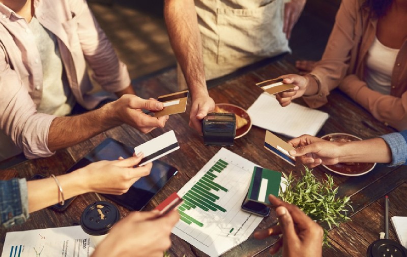 Mâini, carduri de credit, prieteni într-o cafenea, efectuând o plată sau o tranzacție bancară la un terminal POS.