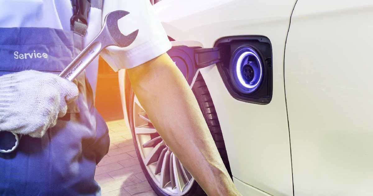 Un mecanic, avnd o cheie în mână, se află lângă o mașină electrică