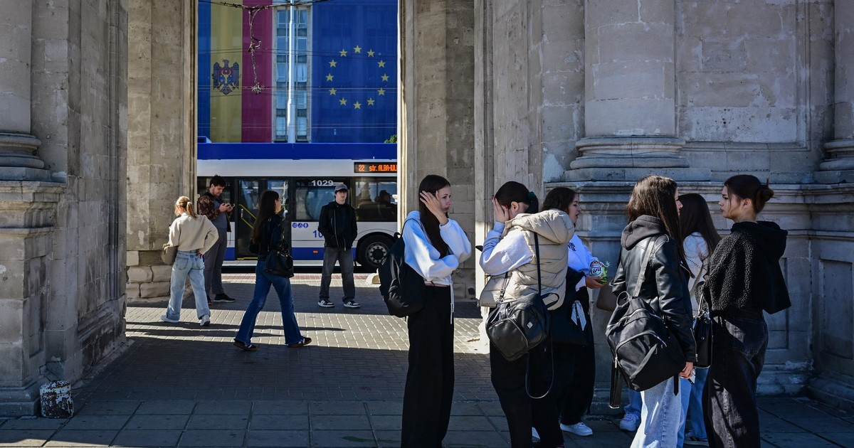 Tineri sunt fotografiați lângă Arcul de Triumf, în timp ce steagurile Moldovei și UE sunt văzute pe clădirea Guvernului din Chișinău, pe 26 septembrie 2025, înaintea alegerilor parlamentare