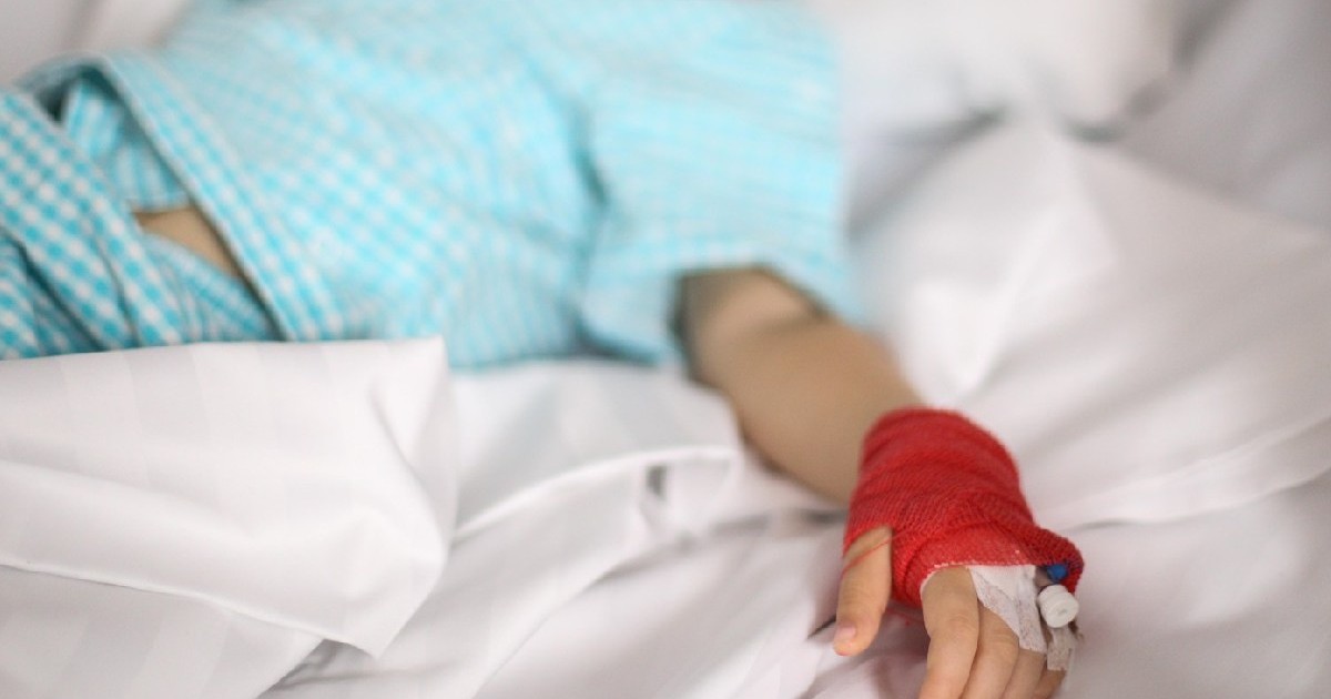 o canulă pe mâna unei fetițe bolnave, care stă pe un pat, într-un spital