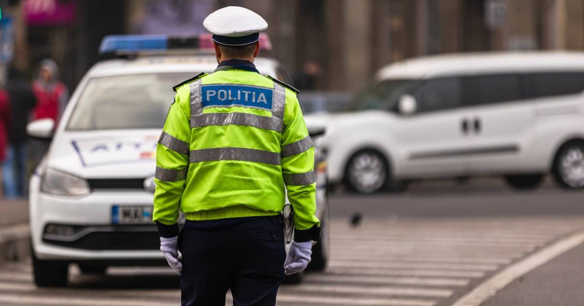 politist imbracat in uniforma in fata lui este autospeciala de politie