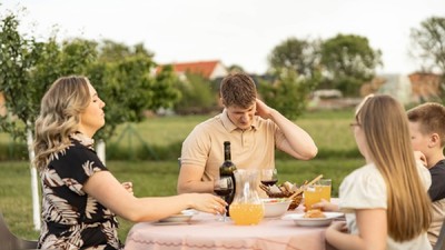 Cum scapi de ţânţari fără a folosi insecticid - O familie cu doi copii se bucură de o masă în grădină, însă tatăl este deranjat de mușcăturile de țânțari și este surprins în timp ce se scarpină pe ceafă