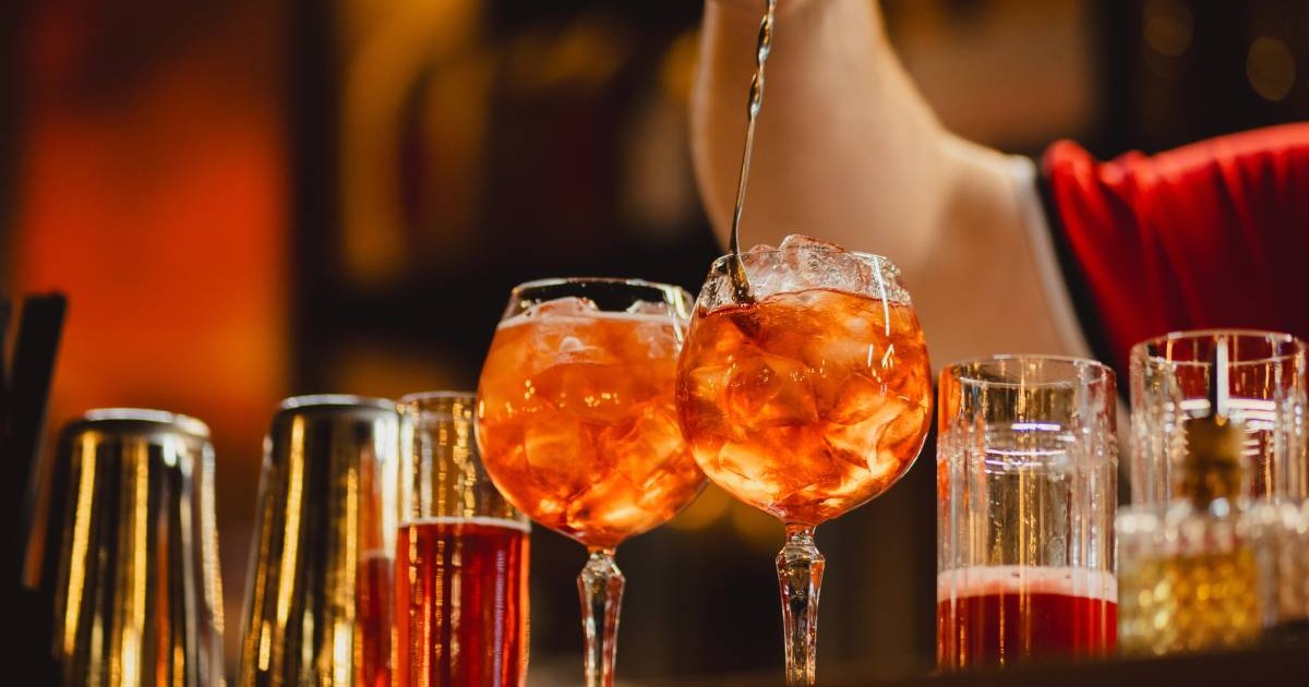 Un barman care pregătește două cockteiluri cu gheață, amestecă în pahar cu o linguriță cu coada foarte lungă