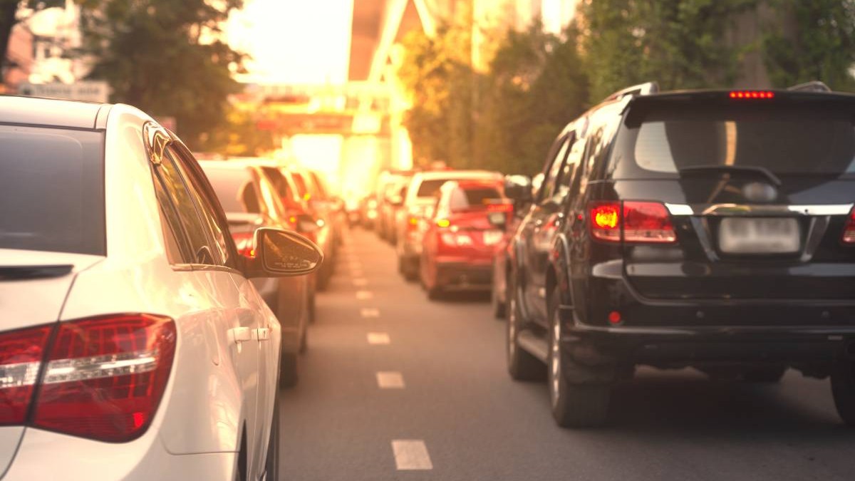 mai multe masini in trafic, pe un drum cu doua benzi pe sens, posibil intr-un oras, in prim plan este o masina neagra