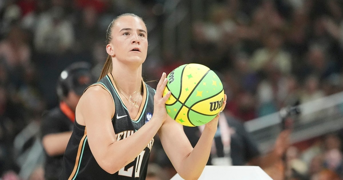 Sabrina Ionescu surprinsă în timp ce ține în mâini mingea și se pregătește să arunce la coș. Poartă un echipament negru cu auriu