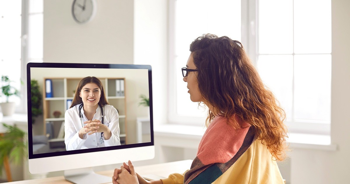 O femeie cu parul lung si ochelari cu un pulover galben sta in fata computerului di priveste la o femeie in halat alb, medic.Telemedicina nu e decontata la medicul de familie. Teleconsultatie. Romani din rural fara acces la servicii medicale. Foto; Shutterstock