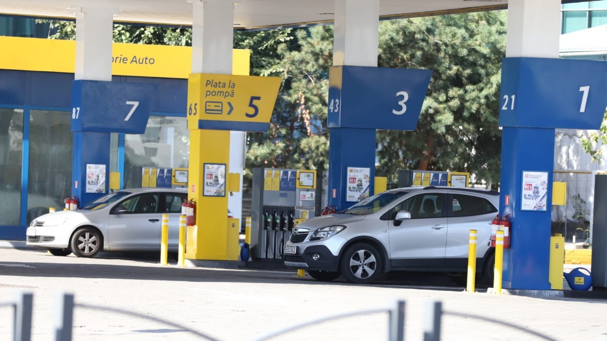 Imaginea prezintă o stație de carburanți cu mai multe pompe numerotate, unde sunt parcate două autoturisme pentru alimentat.