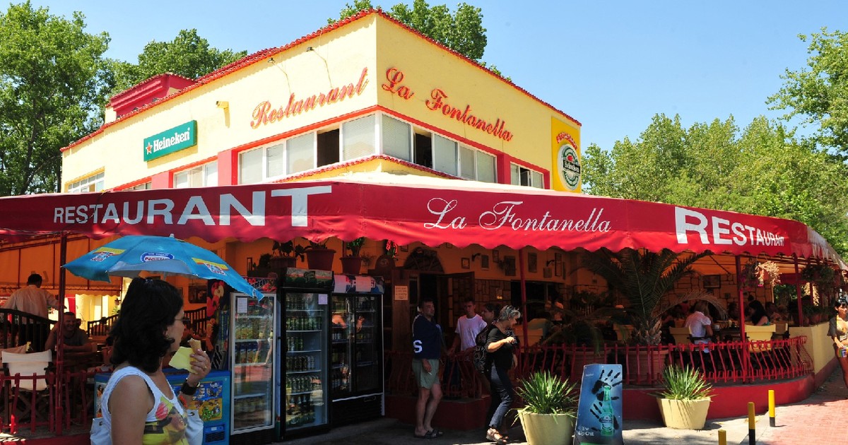 Imaginea surprinde terasa animată a restaurantului „La Fontanella” din Mamaia, cu oameni relaxându-se la mese sub o copertină roșie, într-o zi însorită de vară