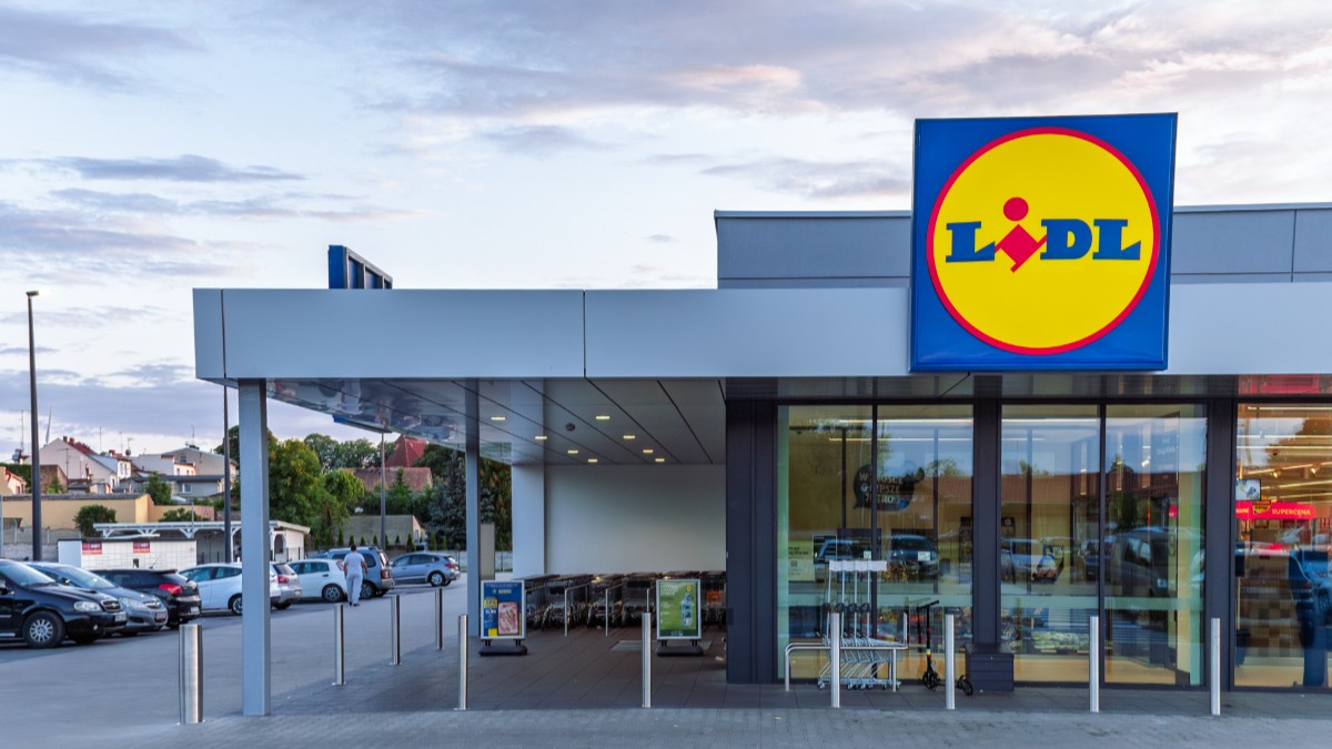 Un magazin Lidl, parcare este plină de mașini, iar la intrare sunt câteva cărucioare goale