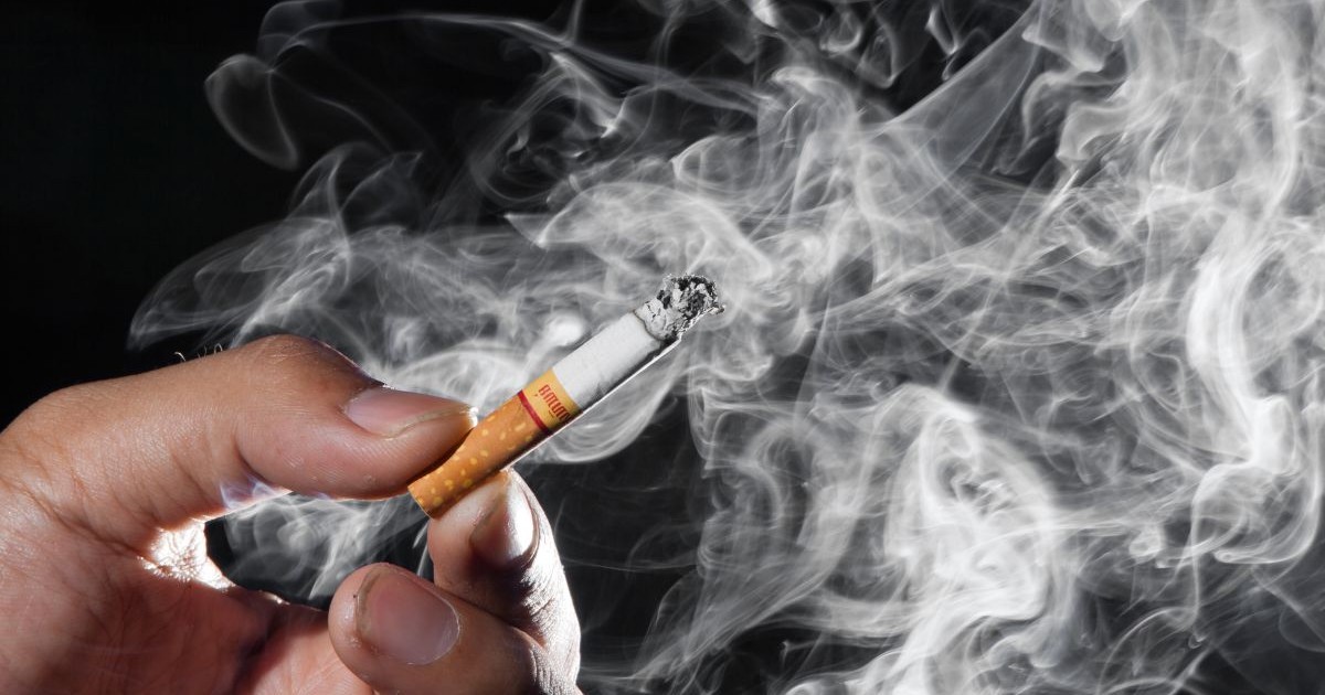 Fum mult care iese de la o țigară aprinsă pe un care un bărbat o ține în mână. Foto: Shutterstock