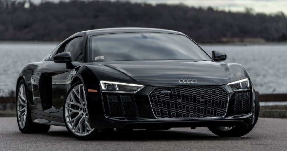 Fotografie cu o mașină sport Audi R8 negru, elegant, parcat pe o suprafață gri, cu un lac și o pădure în fundal