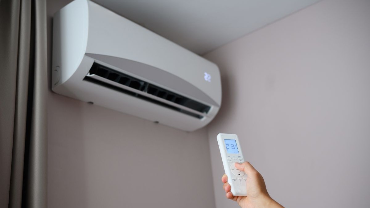 O persoană ține telecomanda în fața unui aparat de aer condiționat, reglându-și temperatura. Omul setează aerul condiționat la o temperatură confortabilă de 22 de grade Celsius