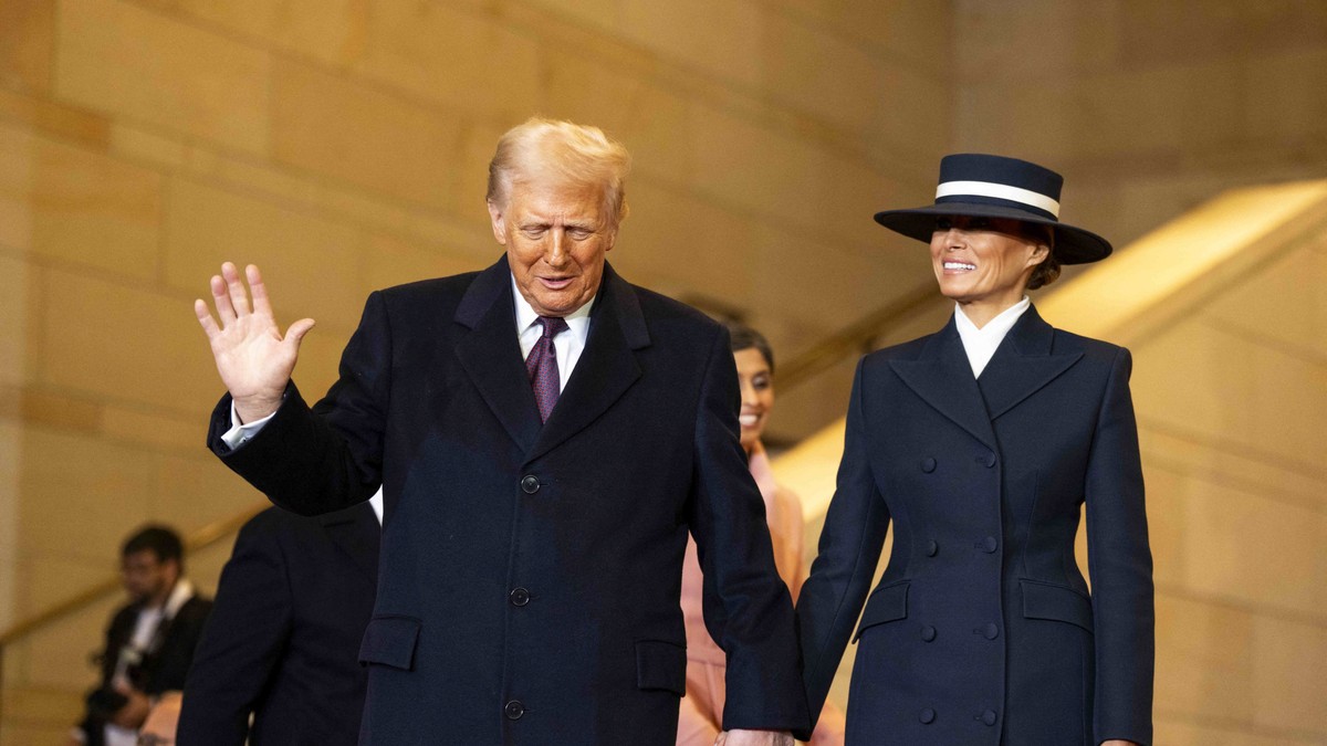 Donald Trump, in stanga, intr-un palton negru, insotit de sotia sa - Melania - care poarta o tinuta neagra si o palarie neagra cu banda alba