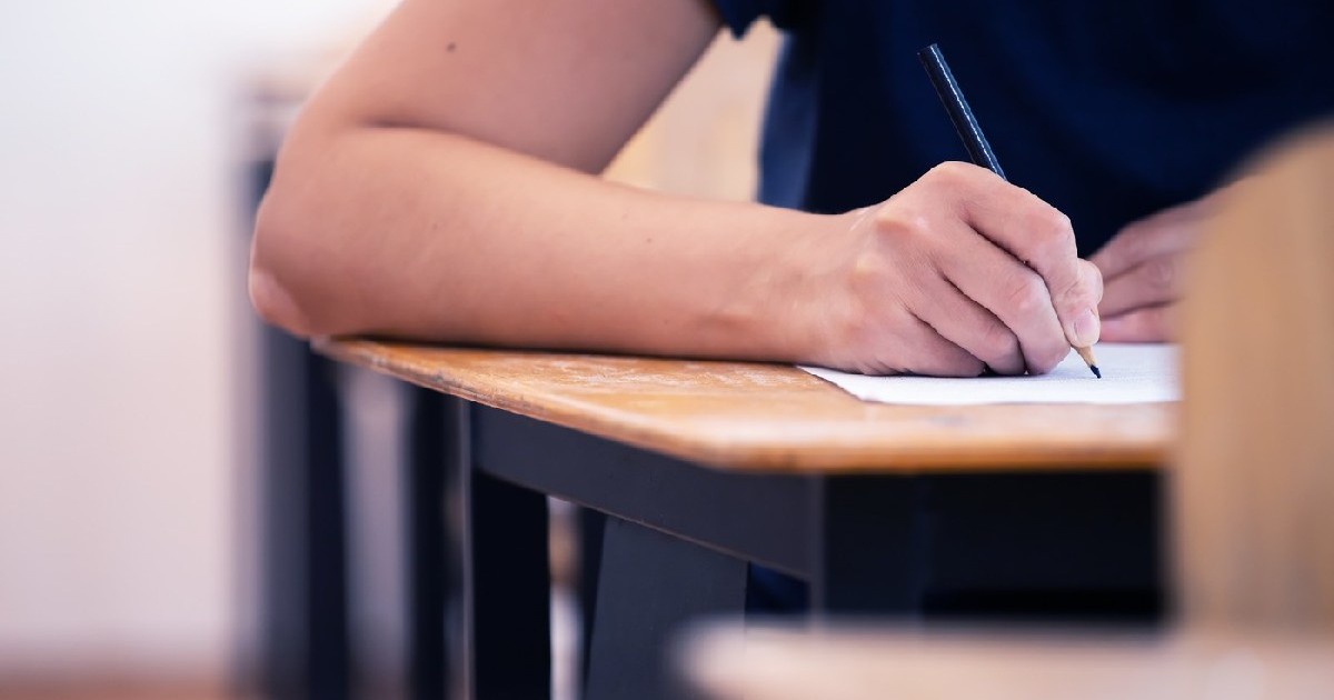 Elev de liceu sau universitate care ține creionul scriind pe foaia de răspuns de hârtie. Concept de examen final.
