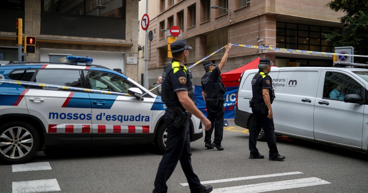 Polițiști care au izolat o zonă stradală cu bandă de securitate în urma unui incident. La fața locului sunt prezenți mai mulți ofițeri în uniformă, o mașină de poliție și o dubă albă de servicii funerare (Serveis Funeraris Barcelona), indicând gestionarea unei scene de crimă.