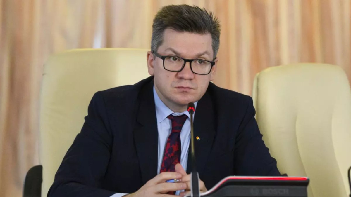 În imagine este ilustrat Mihail Neamțu, îmbrăcat în costum negru, cămașă albastră și poartă o cravată. Acesta stă la un birou, iar în fața sa este un microfon.