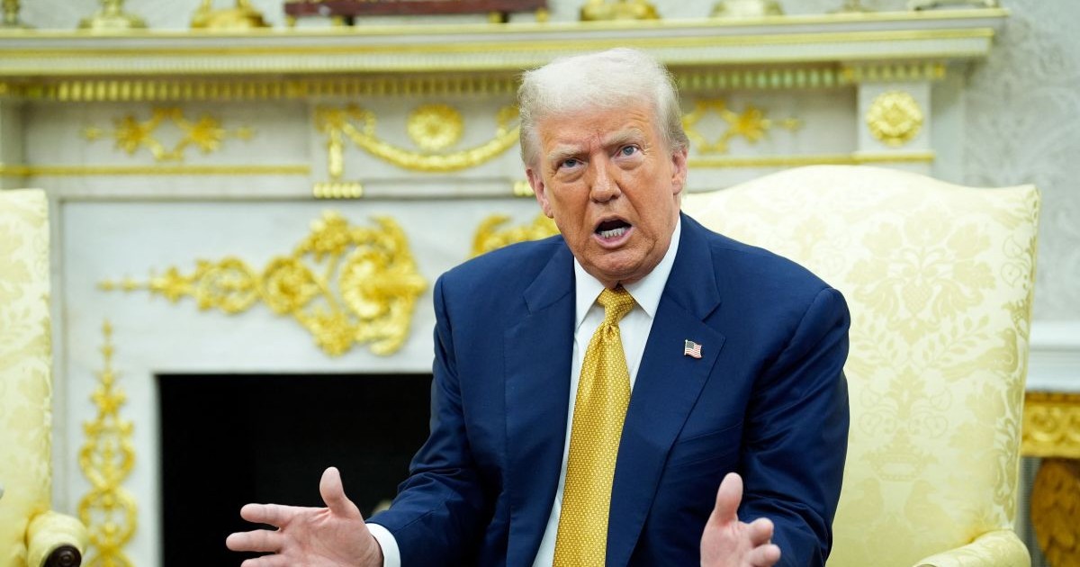 Donald TRump, îmbrăcat la costum și cu cravată galbenă la gât, dă din mâini în timp ce vorbește stând pe un fotoliu de la Casa Albă, iulie 2025