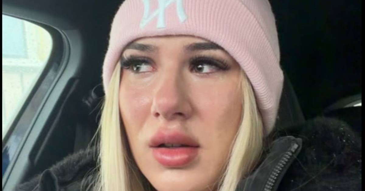 Captura video cu o tanara blonda, cu o caciula roz cu sigla alba, are o geaca neagra, este in interiorul unei masini si plange