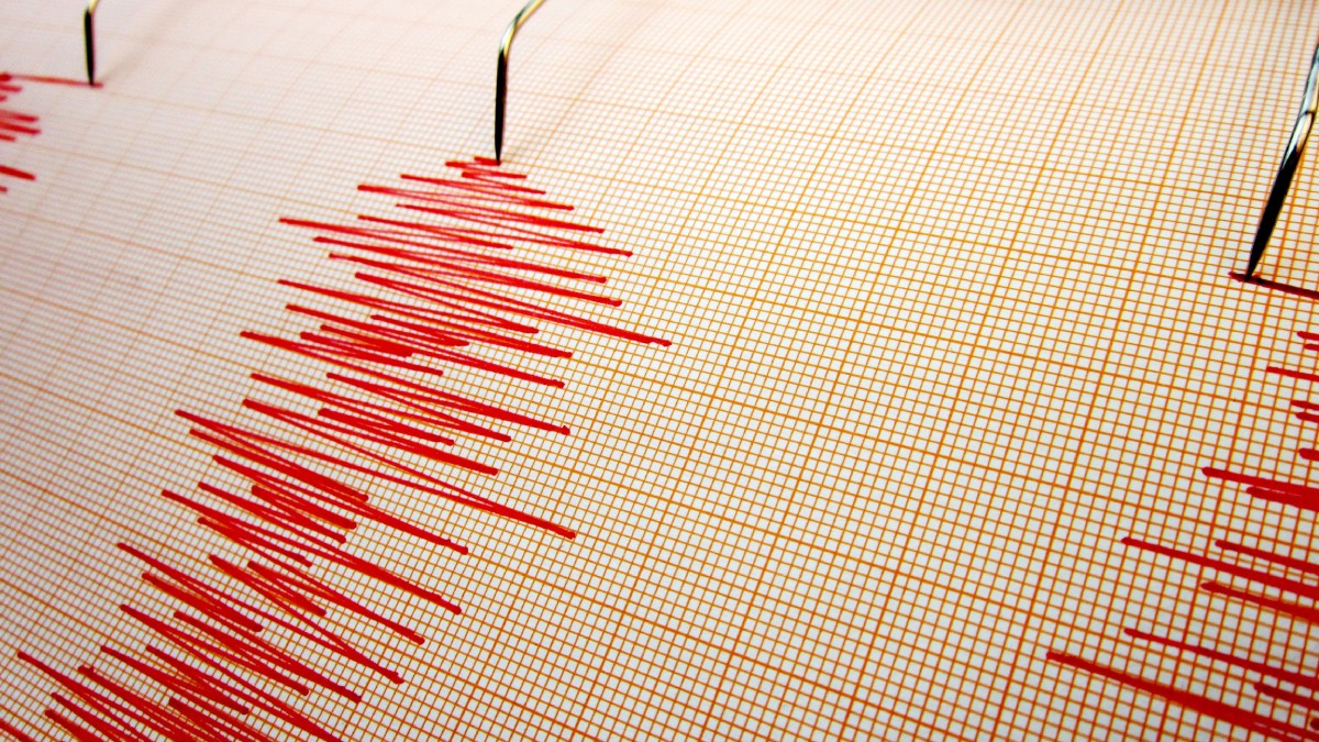 Imaginea arată un seismograf, dispozitiv care înregistrează undele produse de un cutremur, cu linii roșii ce indică intensitatea și durata mișcărilor seismice pe o hârtie milimetrică