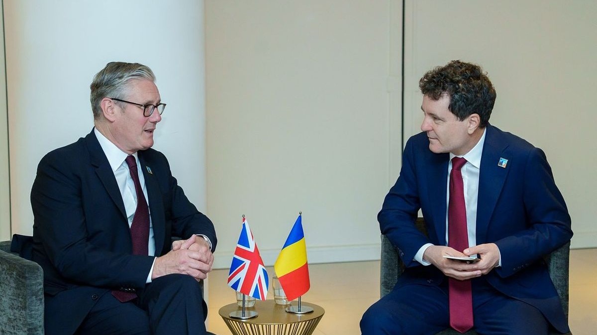 Nicușor Dan discută cu prim-ministrul britanic Keir Starmer stând pe scaune și având în față, pe o măsuță rotundă, steagurile celor două țări
