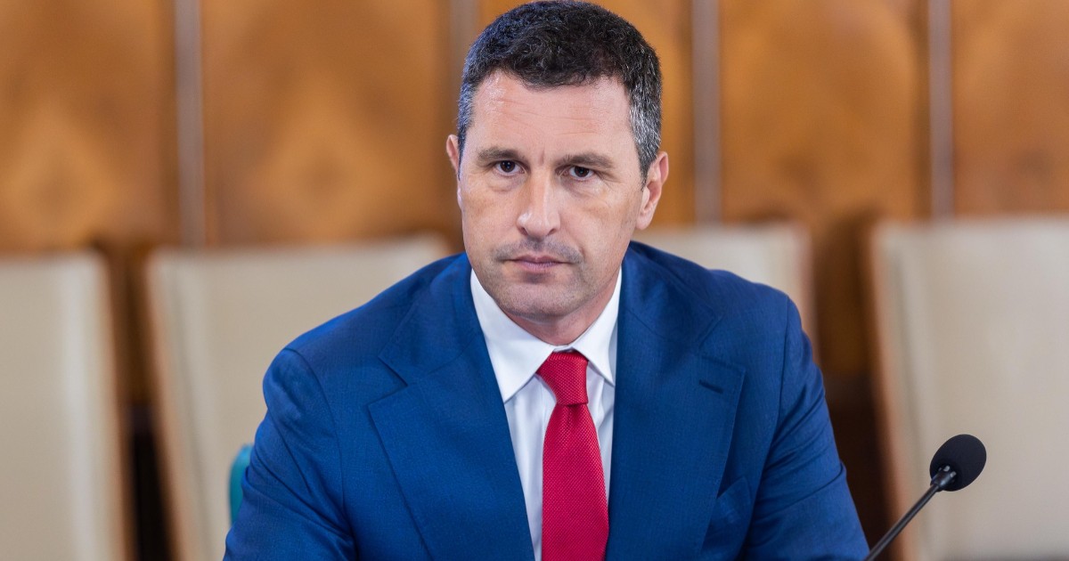 Vicepremierul Tánczos Barna, îmbrăcat într-un costum albastru și cu o cravată roșie, în timp ce stă la masă în timpul unei ședințe de Guvern, la Palatul Victoria