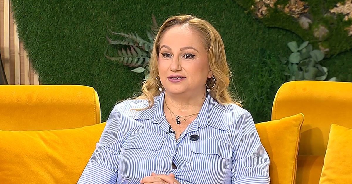 Astrologul Cristina Demetrescu, îmbrăcată cu o rochie cu dungi alb-albastru, fotografiată surprinsă, în timp ce stă pe o canapea portocalie, în studioul unei emisiuni tv, București, 15 septembrie 2025