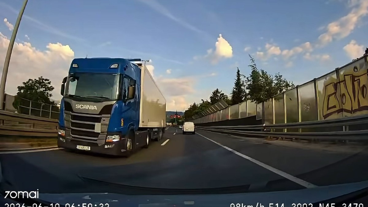 O captură realizată de o cameră de bord pe o autostradă, înfățișând în plan apropiat un camion Scania de culoare albastră cu remorcă albă care circulă pe contrasens.