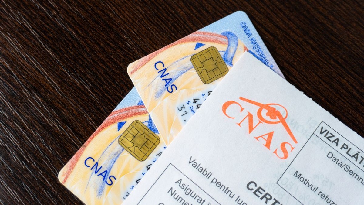 Imagine creativă cu două carduri de sănătate acoperite de o rețetă cu logo-ul CNAS, pe un birou negru